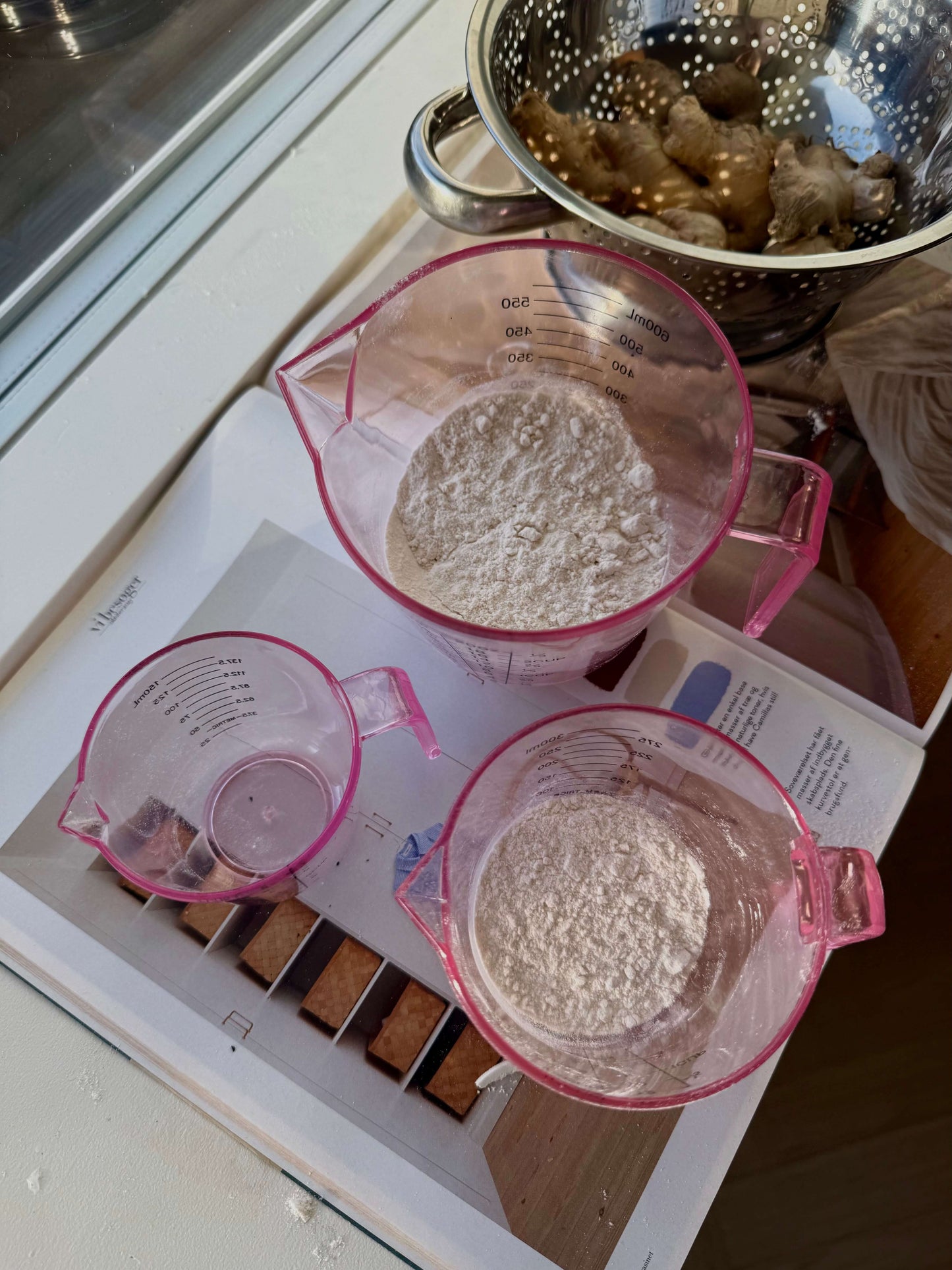 Tre lyserøde målebægre fyldt med mel, klar til madlavning
