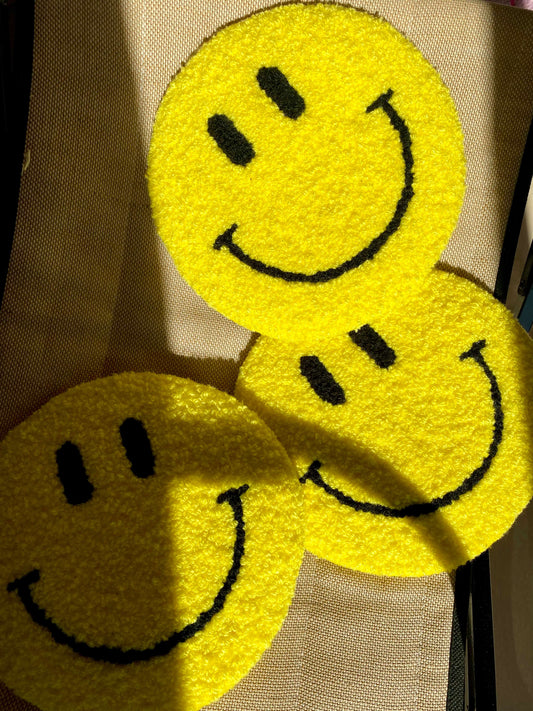 Tre gule Smiley vægtæpper med sorte ansigtstræk – stablet og oplyst af sollys.