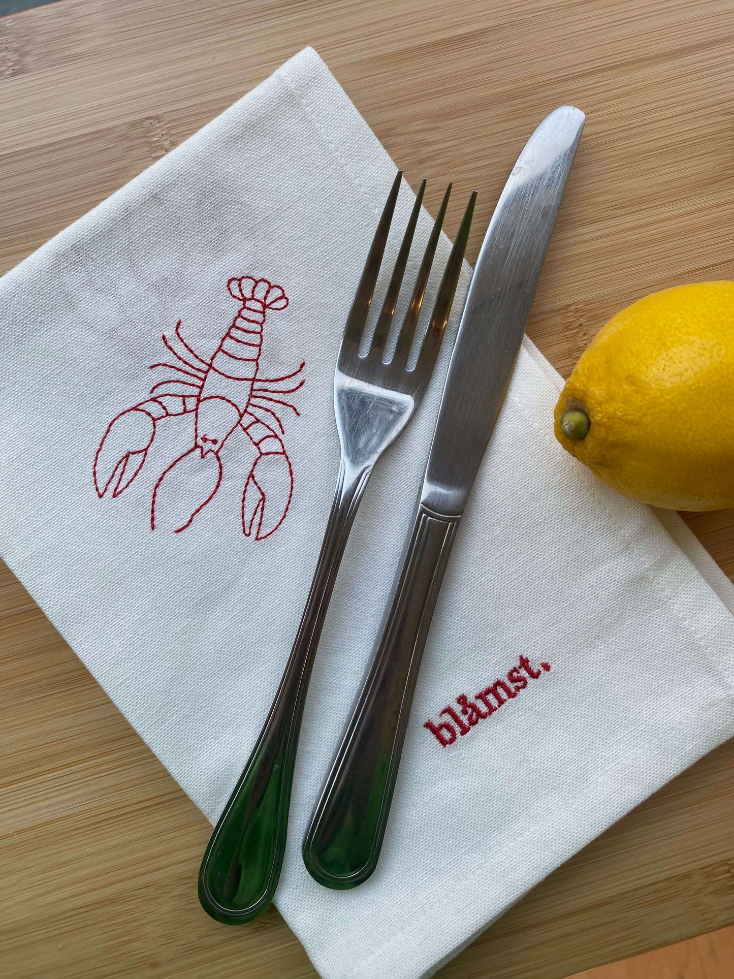 Håndbroderet hummer stofserviet på bord med bestik og citron