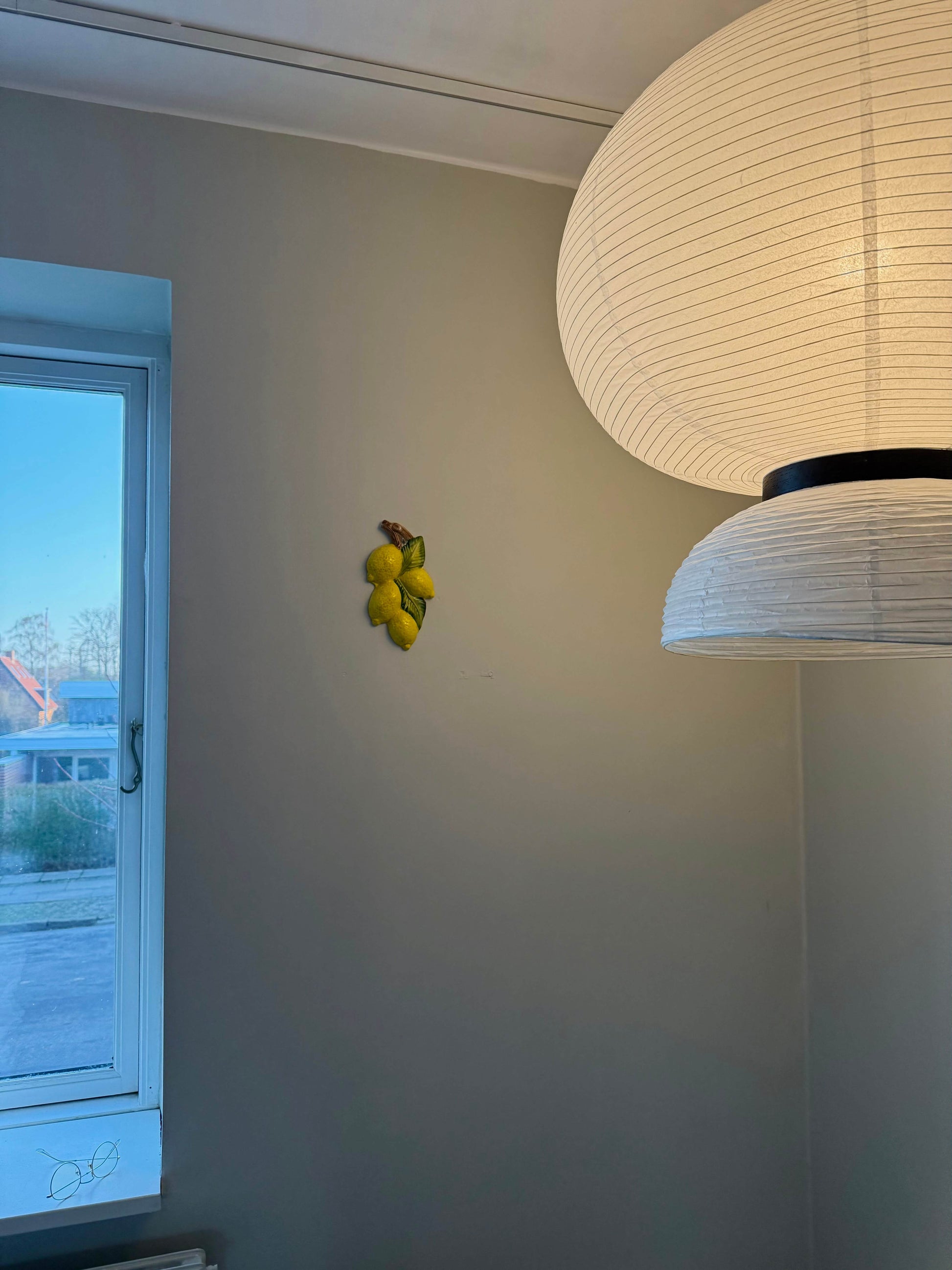 Keramikcitroner som vægdekoration, placeret ved siden af et vindue og en lampe.