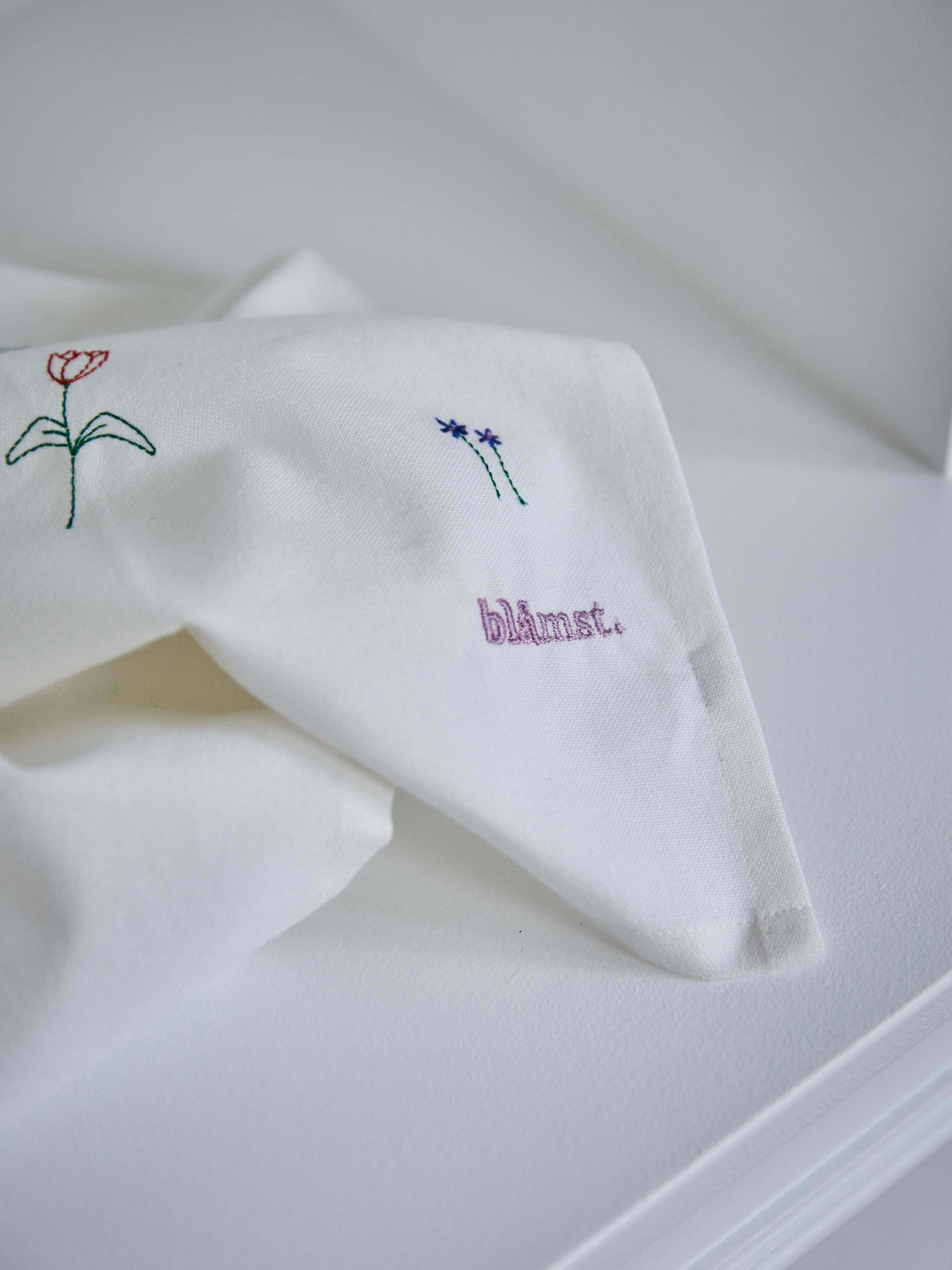 Foldet stofserviet med broderede blomster, lagt på en hvid overflade.