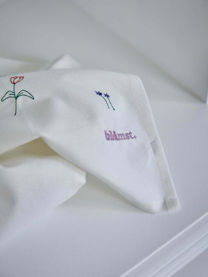 Foldet stofserviet med broderede blomster, lagt på en hvid overflade.