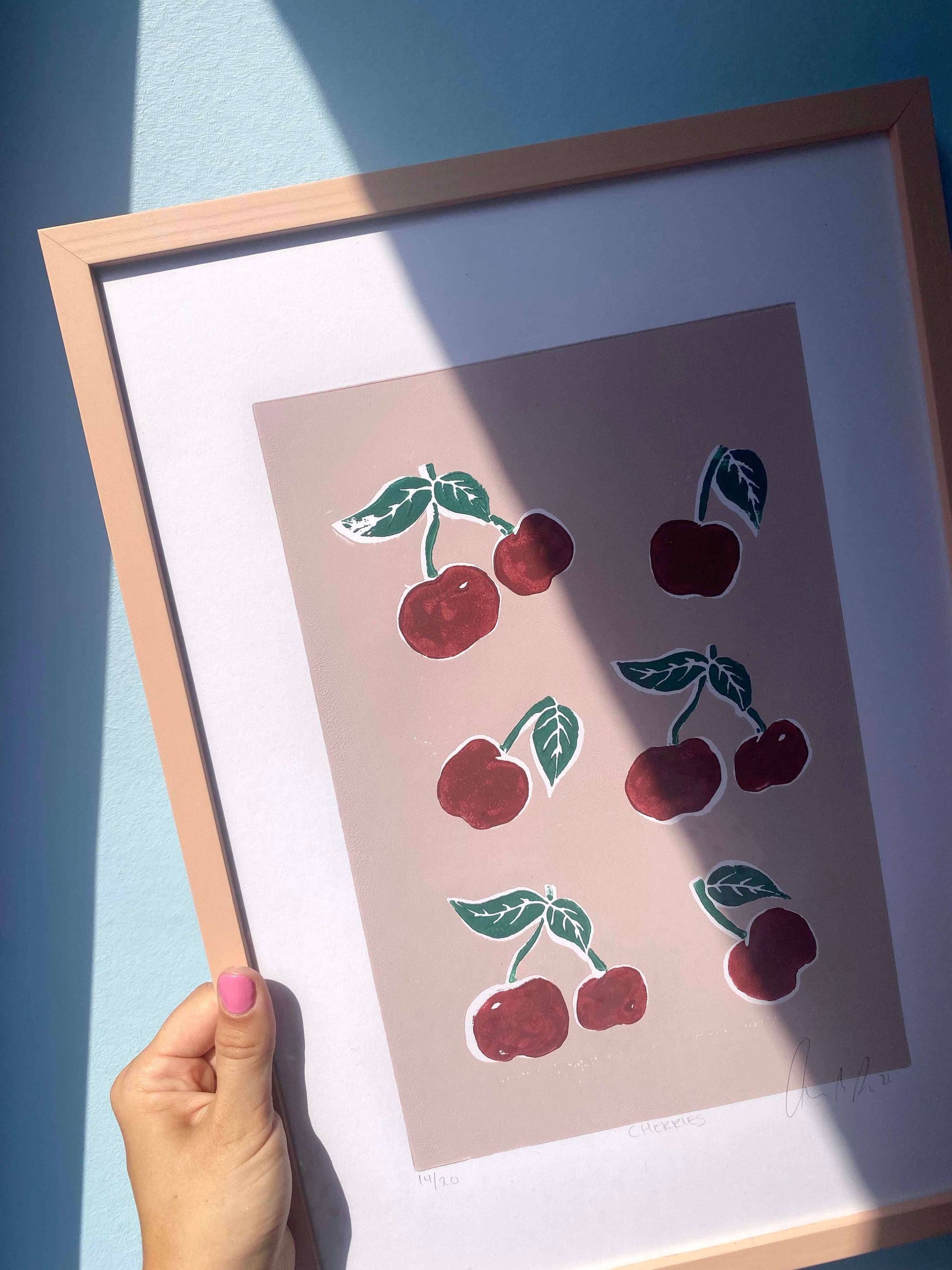 Nærbillede af CHERRIES linoleumstryk i ramme med sollys på blå baggrund.