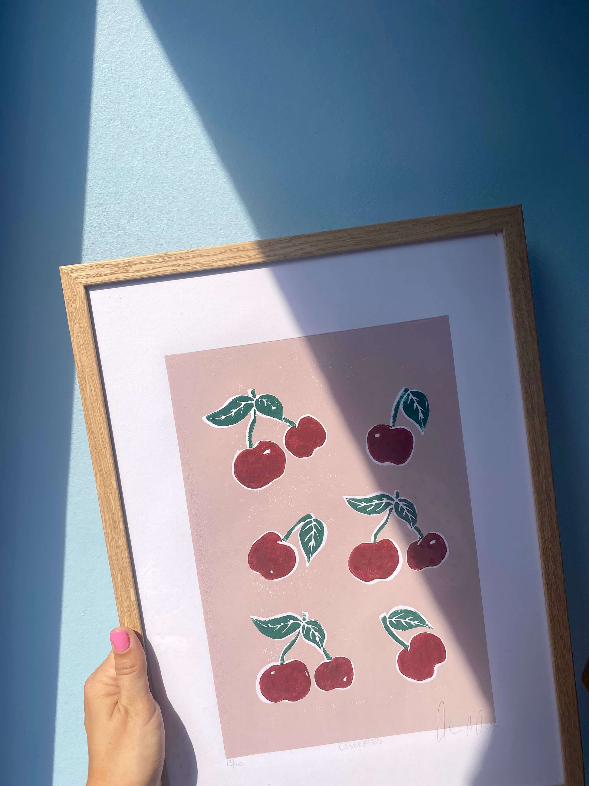 Nærbillede af CHERRIES linoleumstryk i ramme med sollys på blå baggrund.