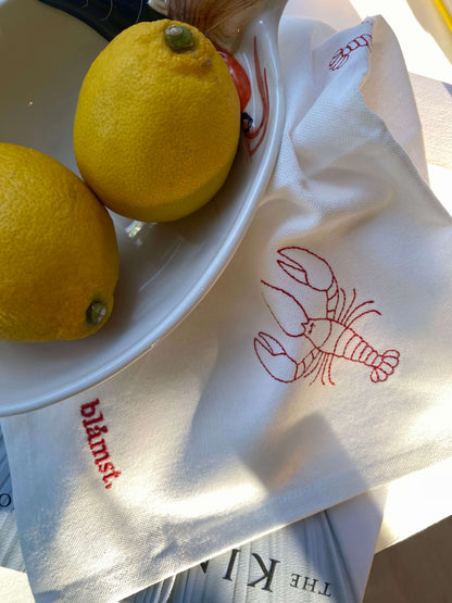 Nærbillede af hummer broderi på stofserviet med citron som dekoration